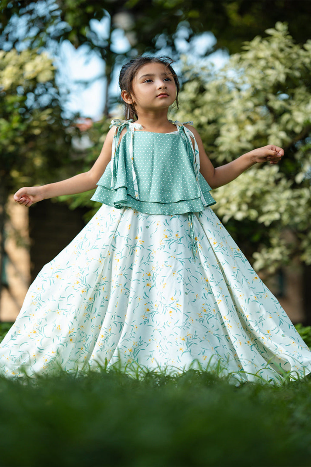 Young girl in a light blue dress standing outdoors with greenery in the background