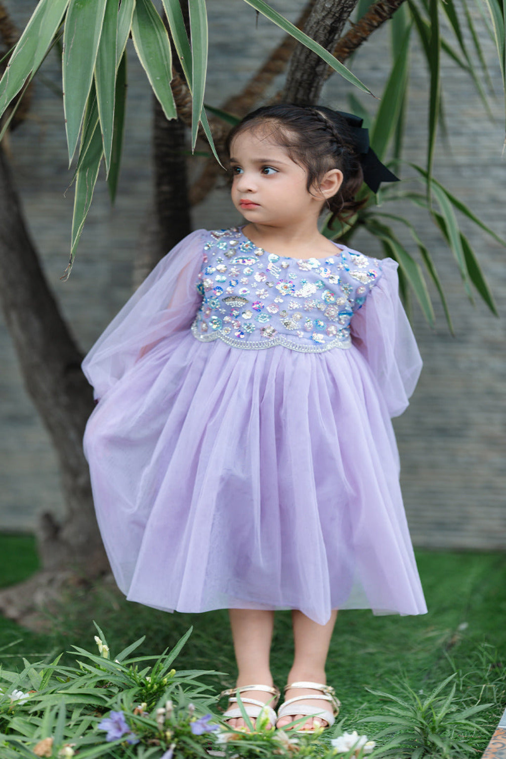 Young girl in a lavender dress with sequin details standing outdoors.