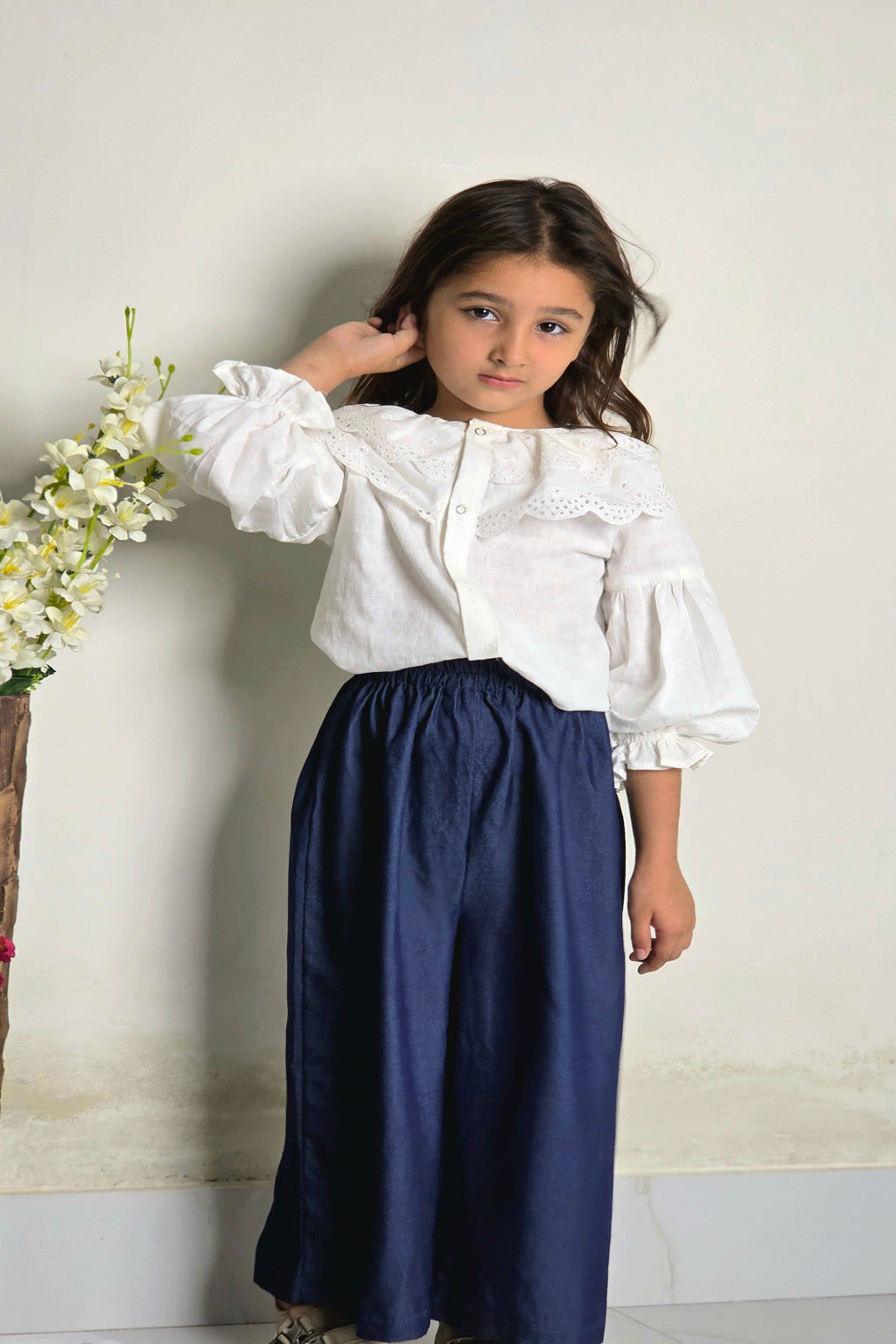 Young girl wearing a white blouse and navy skirt against a plain background