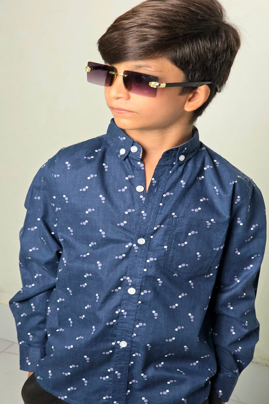 Child wearing a navy blue shirt with white patterns and sunglasses against a plain background