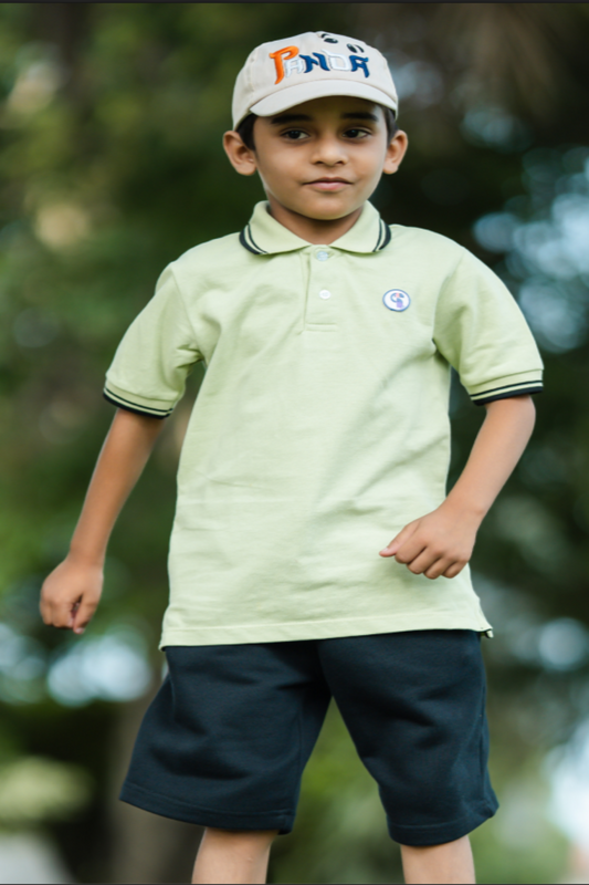 Child wearing a light green polo shirt and dark shorts with a blurred natural background