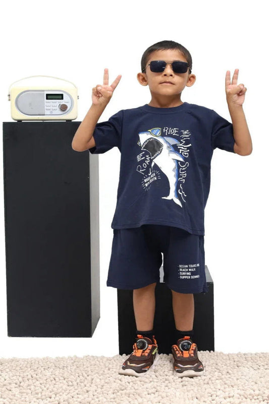 Child wearing a navy blue t-shirt with a shark design, standing next to a black speaker and white radio.