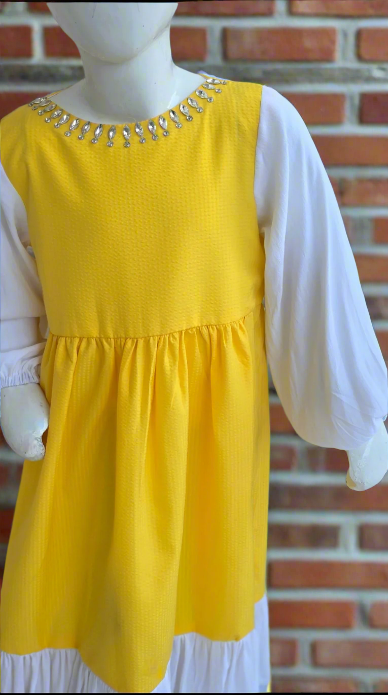 Yellow dress with white sleeves on a mannequin against a brick wall.