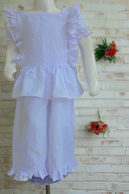 White dress with ruffled details on a mannequin against a white brick wall with floral decorations.