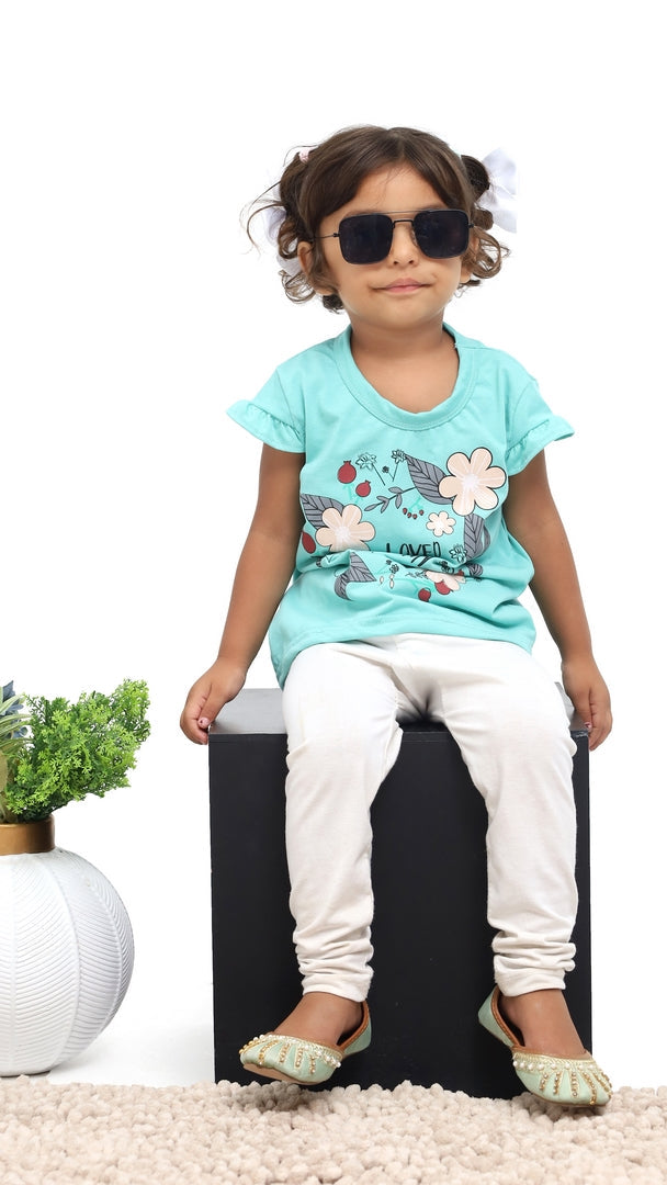 Child wearing a light blue t-shirt with a floral design and white pants, sitting on a black box.
