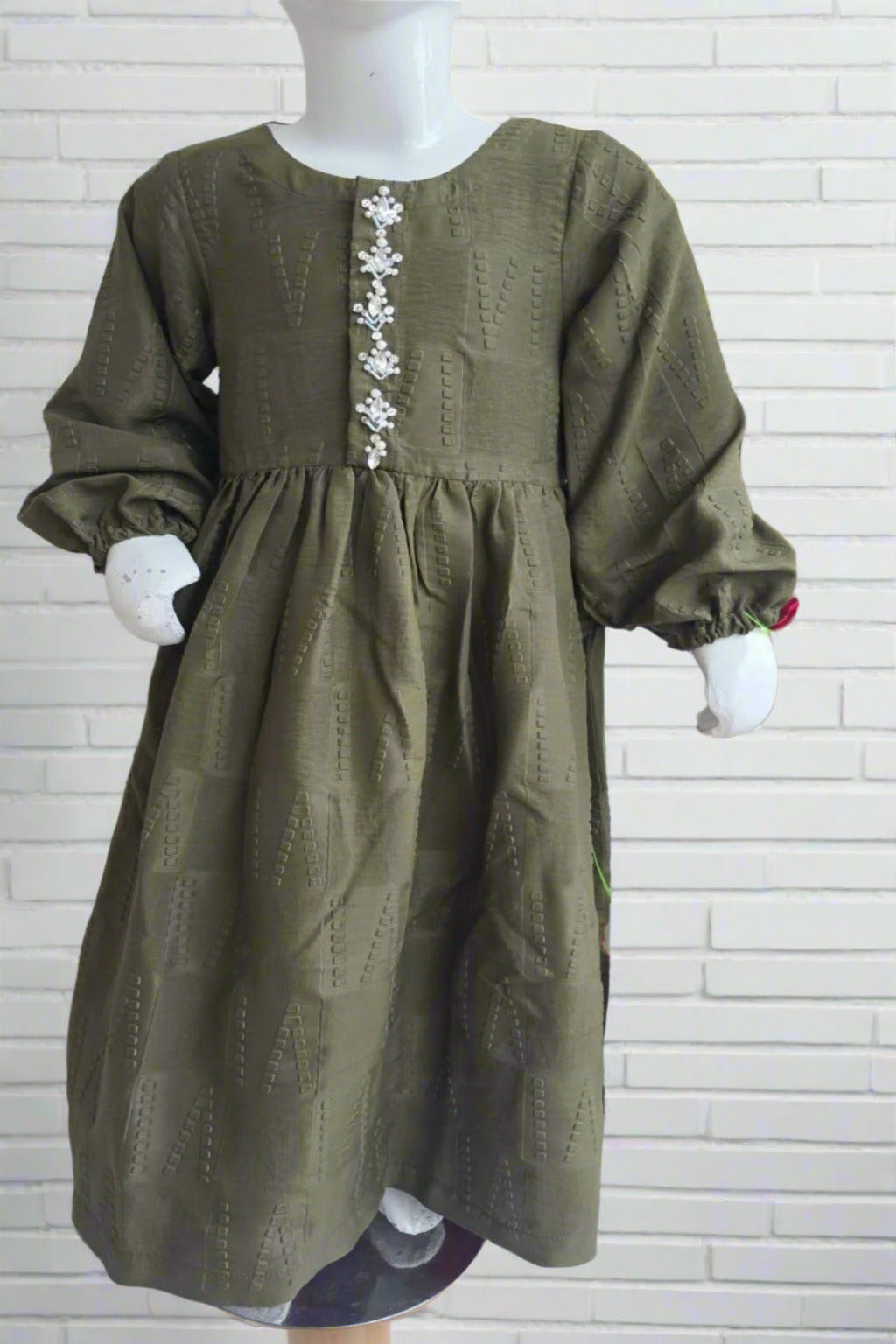 Green dress with floral embellishments on a mannequin against a white brick wall.