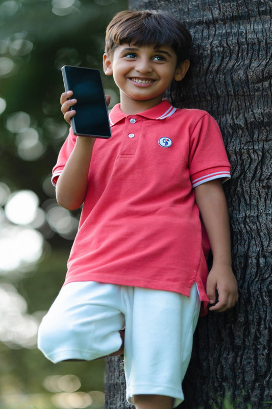 Child in a pink shirt holding a smartphone next to a tree