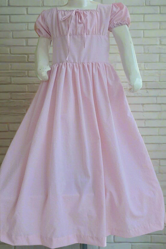 Pink dress on a mannequin against a white brick wall with flowers.
