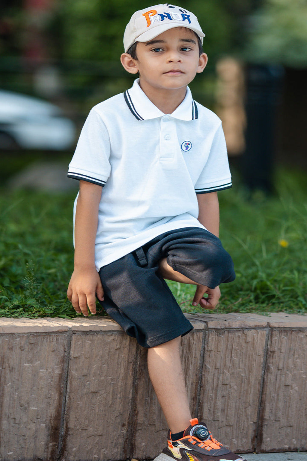 Child sitting on a stone wall wearing a white polo shirt and dark shorts with a blurred background